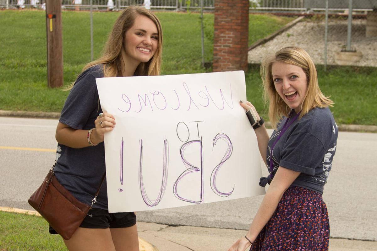 两名女学生举着写着“欢迎来到SBU”的广告牌